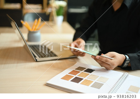 Young interior designer man holding color swatches and using laptop, working for new project at creative office 93816203