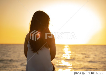 水平線に沈む夕日を眺める女性の後姿の写真素材 [93816325] - PIXTA