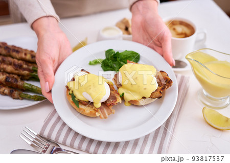 Tasty eggs Benedict, hollandaise sauce and aspargus covered with bacon Tasty eggs Benedict, hollandaise sauce and aspargus covered with bacon 93817537