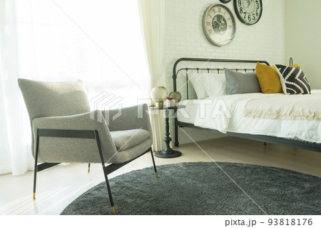 Modern grey armchair next to bed with grey pillows in bedroom interior with large clock on wall. Modern grey armchair next to bed with grey pillows in bedroom interior with large clock on wall. 93818176