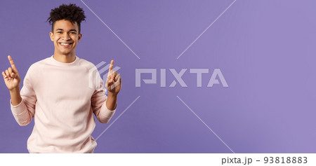 Waist-up portrait of joyful good-looking hispanic man with dreads, promoting product or company banner hanging on top, pointing fingers up, smiling satisfied, recommend subscribe or click link 93818883