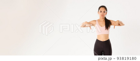 Sport, wellbeing and active lifestyle concept. Upset and disappointed asian sportswoman, woman in fitness clothing pointing fingers down with sulking face, complaining on banner, white background Sport, wellbeing and active lifestyle concept. Upset and disappointed asian sportswoman, woman in fitness clothing pointing fingers down with sulking face, complaining on banner, white background 93819180