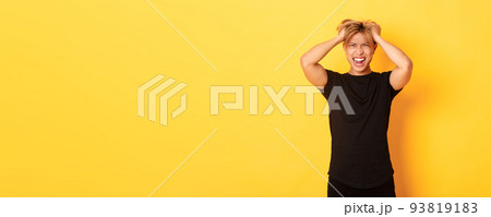 Portrait of pissed-off angry asian man tossing haircut and yelling furious, standing over yellow background 93819183