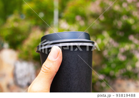 Black paper cup of coffee in hand on park background Black paper cup of coffee in hand on park background 93819488