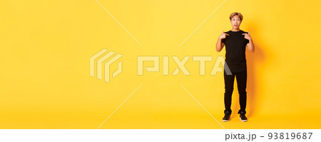 Full-length of surprised attractive korean blond guy in black outfit pointing at himself impressed, yellow background Full-length of surprised attractive korean blond guy in black outfit pointing at himself impressed, yellow background 93819687