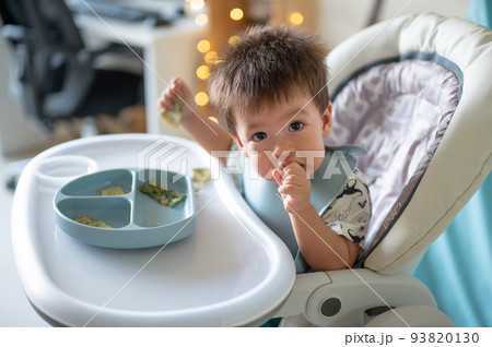 Baby boy eating by himself in his high chair at home Baby boy eating by himself in his high chair at home 93820130