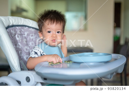 Baby boy eating by himself in his high chair at home 93820134
