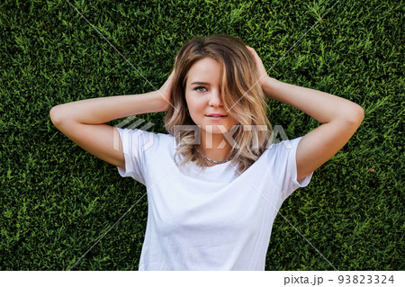Young woman in white shirt with natural makeup standing by green hedge 93823324