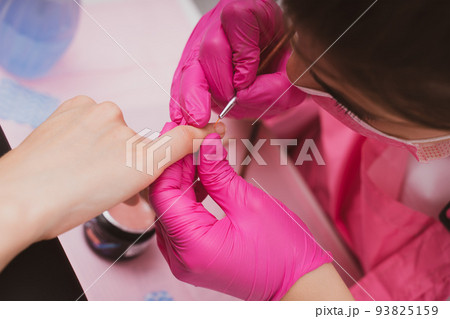 Manicure salon master drawing varnish on the nail tip with a thin brush. Professional manicure in Manicure salon master drawing varnish on the nail tip with a thin brush. Professional manicure in 93825159