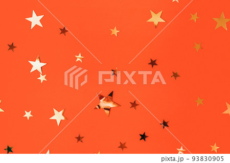 Golden stars glittering confetti on red background. Trendy festive holiday backdrop. Many star-shaped particles for a postcard, invintation or web banner. 2023 merry xmas backplate 93830905
