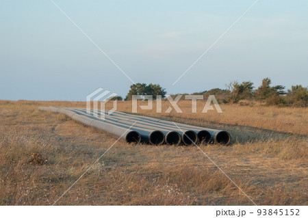 Pipes for laying water pipes lie on the lawn. Sunset, the rays of the sun illuminate the construction site 93845152