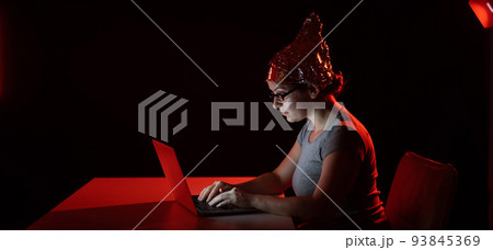 Paranoid caucasian woman typing on a computer wearing a tinfoil cap. Conspiracy theory. Paranoid caucasian woman typing on a computer wearing a tinfoil cap. Conspiracy theory. 93845369