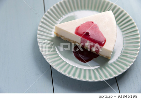 木製テーブルの上のブルーベリーソースがかかったレアチーズケーキ 93846198