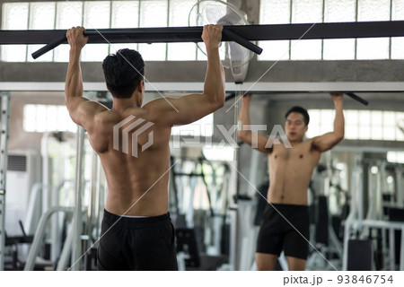 Muscular Asian man pulling up on horizontal bar in gym 93846754
