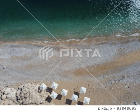 Aerial view from above on azure sea and pink pebbles beach. Small waves on cristal clear water surface in motion blur. Summer ocean sea beach background. Nobody. Holiday, vacation and travel concept Aerial view from above on azure sea and pink pebbles beach. Small waves on cristal clear water surface in motion blur. Summer ocean sea beach background. Nobody. Holiday, vacation and travel concept 93848695