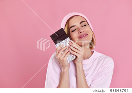 woman enjoying dark chocolate on pastel pink background 93848792