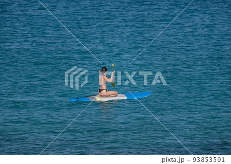 A girl with an oar floats on a board on the sea 93853591