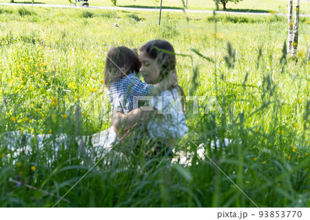 Brother and sister are playing in the park among the green grass. Children hug tightly. Picnic outside the city. Childhood. Relationships. 93853770
