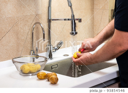 A man peels potatoes on the skin in the kitchen and puts them in a basket 93854546