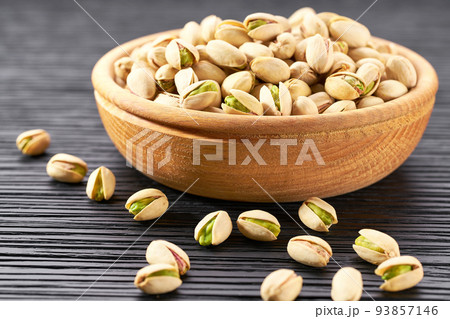 Pistachios in wooden bowl on black table, selective focus. 93857146