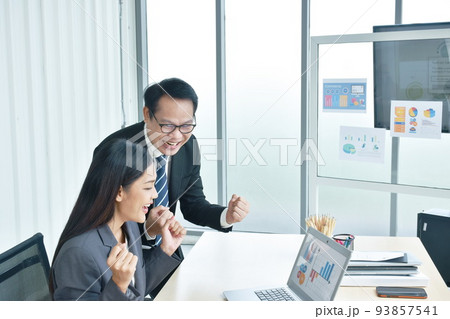 happy busimess Asian man and woman looking at laptop screen with success moment in office happy busimess Asian man and woman looking at laptop screen with success moment in office 93857541
