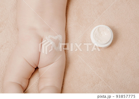 Baby is lying on a white sheets. Baby bum and feet. Mom applying some cream. Close-up of mother hands applying cream under the diaper on little baby pop. 93857775