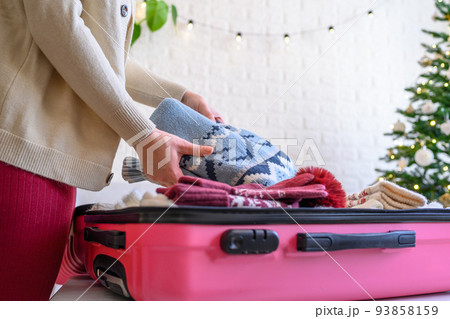 Christmas time. Woman putting knitted winter clothing in a suitcase in the room decorated christmas tree. Travel, holiday Christmas time. Woman putting knitted winter clothing in a suitcase in the room decorated christmas tree. Travel, holiday 93858159