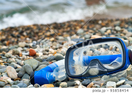 Blue snorkel and mask for diving on the pebble beach. Blue snorkel and mask for diving on the pebble beach. 93858454