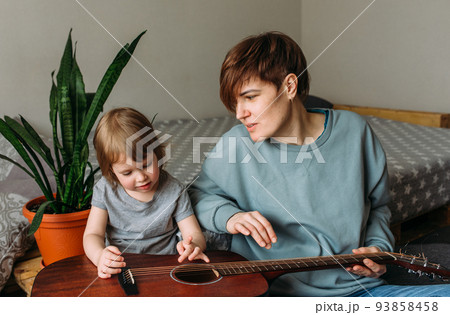 Little girl plays the guitar with her mother on the floor at home Little girl plays the guitar with her mother on the floor at home 93858458
