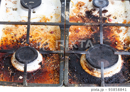 Dirty gas stove surface. Four gas burners and cast iron grate of a gas oven surrounded by old leftovers of food and drinks. Top area surface and burner heads needs cleaning from burnt-on grease Dirty gas stove surface. Four gas burners and cast iron grate of a gas oven surrounded by old leftovers of food and drinks. Top area surface and burner heads needs cleaning from burnt-on grease 93858841