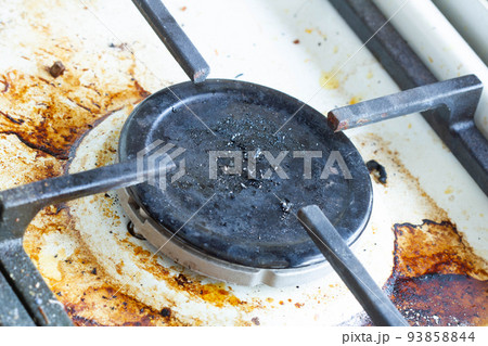 Dirty gas stove surface. Gas burner and cast iron grate of a gas oven surrounded by old leftovers of food and drinks. Top area surface and burner heads needs cleaning from burnt-on grease. Close-up Dirty gas stove surface. Gas burner and cast iron grate of a gas oven surrounded by old leftovers of food and drinks. Top area surface and burner heads needs cleaning from burnt-on grease. Close-up 93858844