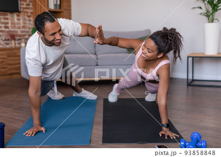 Smiling young african american lady and guy in sportswear doing plank exercises and give high five Smiling young african american lady and guy in sportswear doing plank exercises and give high five 93858848