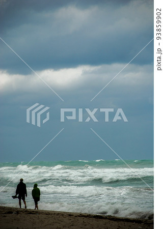 Two people walk on the beach during bad weather Two people walk on the beach during bad weather 93859902