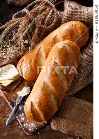 Two freshly baked loaves on wooden cutting board with organic butter and knife. 93860903