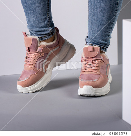 Cropped image of warm pink sneakers with down on female model legs in studio. Cropped image of warm pink sneakers with down on female model legs in studio. 93861573