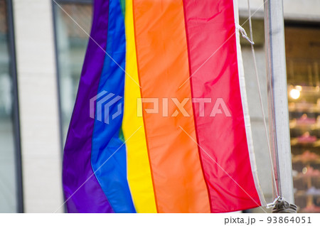 Close-Up rainbow gay pride flag outside on a street. Symbol of the Lesbian Bisexual Transgender LGBT community waving in wind against cloudy sky. Social movement for freedom and equliaty. Copy Space  93864051