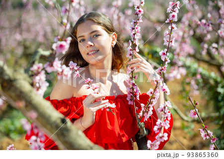 Lady wearing red dress and posing in park with blooming trees 93865360