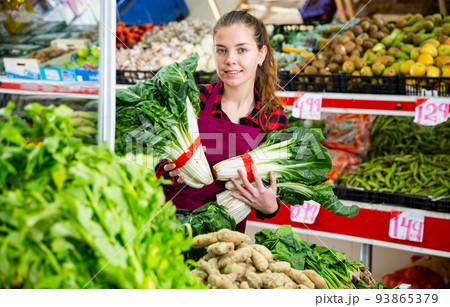 Portrait of a young saleswoman laying out bundles of chinese cabbage on the counter Portrait of a young saleswoman laying out bundles of chinese cabbage on the counter 93865379