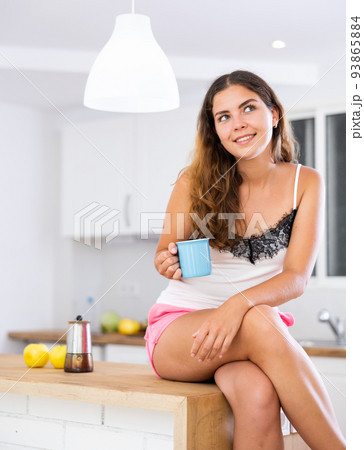 Dreamy girl housewife with a cup of coffee in her hands in modern kitchen 93865884