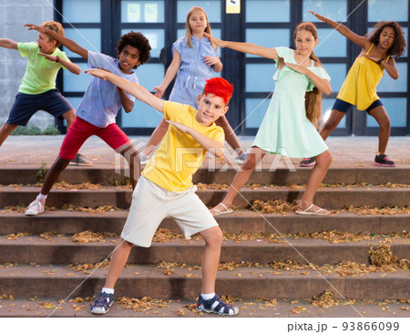 Boy dancing modern choreography with group of tweenagers on city street Boy dancing modern choreography with group of tweenagers on city street 93866099