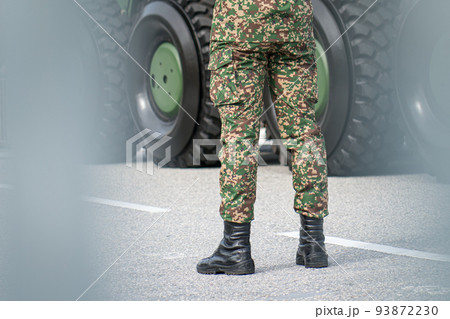 Close up of legs of soldier standing in front of metal tank. Close up of legs of soldier standing in front of metal tank. 93872230