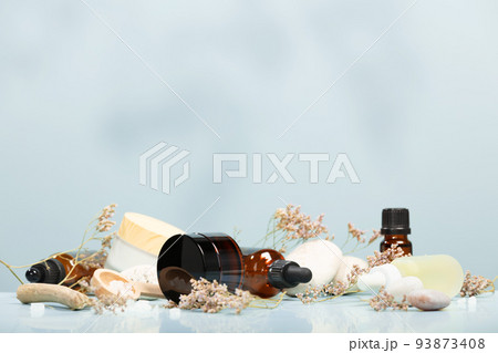 Composition with bottles of essential oils, facial serum, creams on table with stones and flowers on blue background. Natural cosmetics 93873408