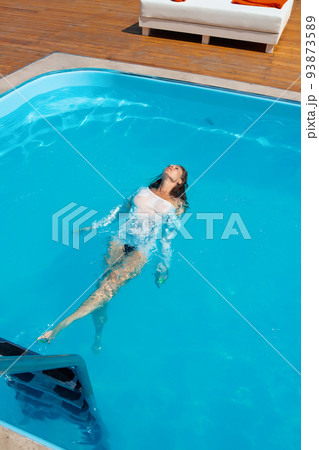Sensual lady in wet dress standing in pool during summer vacation Sensual lady in wet dress standing in pool during summer vacation 93873589