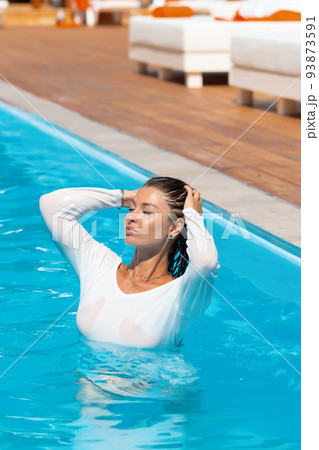 Sensual lady in wet dress standing in pool during summer vacation Sensual lady in wet dress standing in pool during summer vacation 93873591