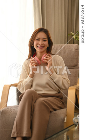 Joyful young woman listening to music on wireless headphone, resting on comfortable couch at home 93876534