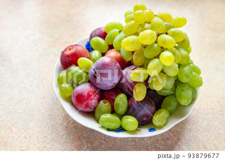 green grapes and plums in a plate on the windowsill, concept of fresh fruits and healthy food 93879677