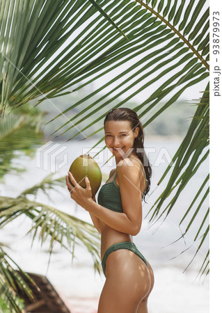 Asian Woman With Coconut Under Palm Tree on the Beach on Summer Vacation Asian Woman With Coconut Under Palm Tree on the Beach on Summer Vacation 93879973