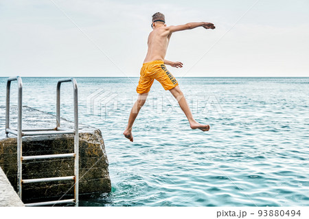 Moments of schoolboy jumping from stone pier with ladder into sea doing tricks in combined image sequence 93880494