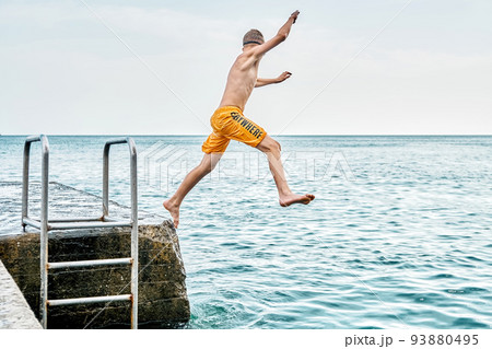 Moments of schoolboy jumping from stone pier with ladder into sea doing tricks in combined image sequence Moments of schoolboy jumping from stone pier with ladder into sea doing tricks in combined image sequence 93880495
