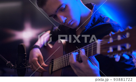 Man plays guitar. Young man plays a musical instrument. Musician records his composition in a music Studio using professional microphone Man plays guitar. Young man plays a musical instrument. Musician records his composition in a music Studio using professional microphone 93881722